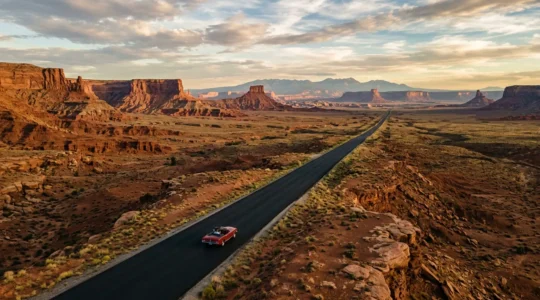 Vue aérienne d'une route emblématique traversant un paysage désertique avec une voiture classique américaine roulant vers l'horizon