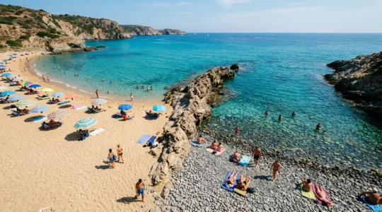 Vue aérienne d'une plage divisée entre sable fin doré et galets polis, avec des parasols colorés et des vacanciers profitant du soleil