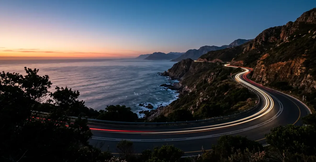 Route côtière de la Garden Route au crépuscule avec phares de voiture éclairant la route sinueuse entre océan et montagnes